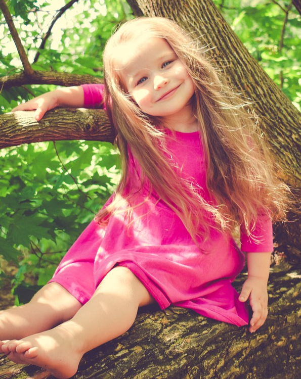Bambina seduta sul ramo di un albero